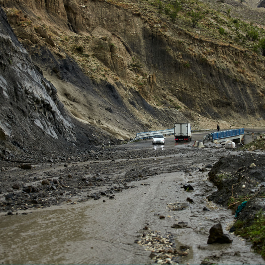 A highway alonside a mountain that has washed out due to mudslide. A truck and 2 cars are covered with mud