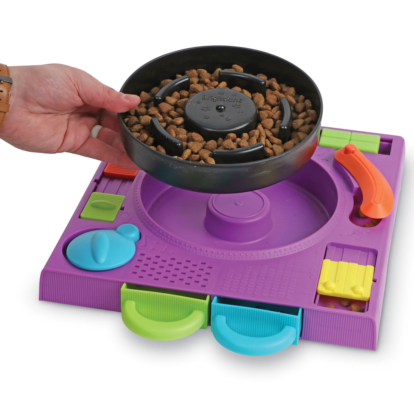 A hand holding the bowl portion of a purple turntable style food puzzle filled with dog food 
