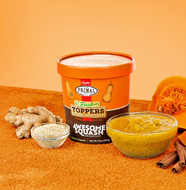 An orange container of squash dog food topper with a bowl full of topper, cinammon sticks, a half a squash, some sesame seeds in a bowl and a bulb of ginger against an orange background