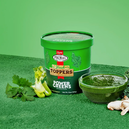 A green container of greens dog food topper beside some celery, parsley, mushrooms and a bowl of the topper, against a green background