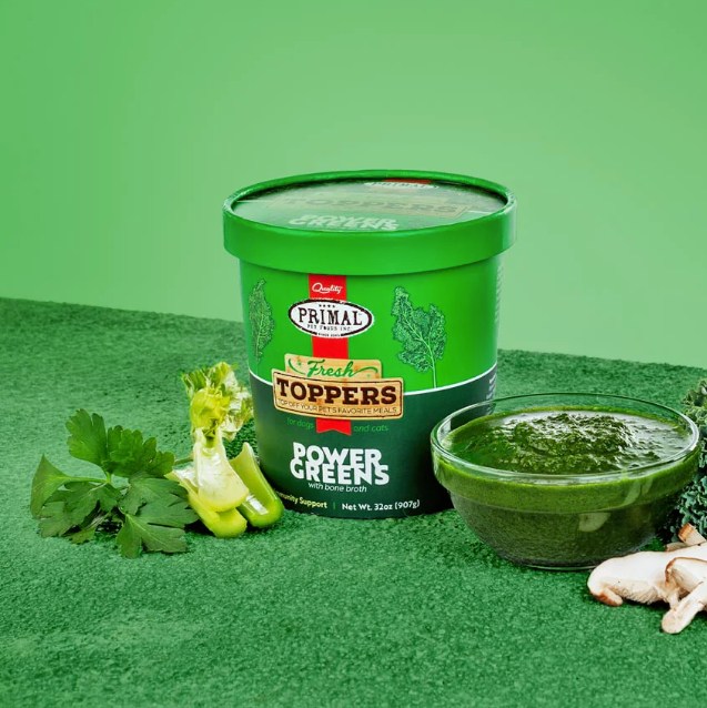 A green container of greens dog food topper beside some celery, parsley, mushrooms and a bowl of the topper, against a green background