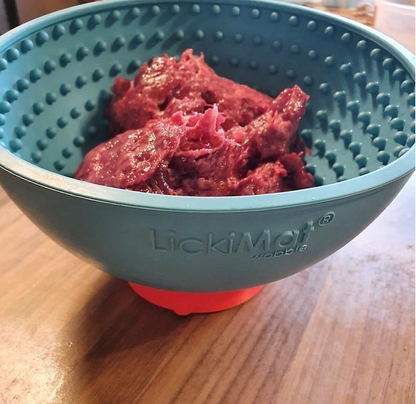 A red rubber ring-shaped stand with a fillable work-to-eat dog bowl on top of it