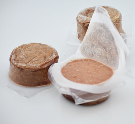 three plastic packs of frozen raw dog food, one opened to reveal the texture of the food
