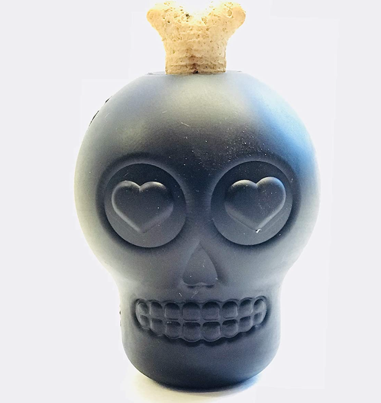 A black rubber skull shaped dog toy with a dog biscuit sticking out of it